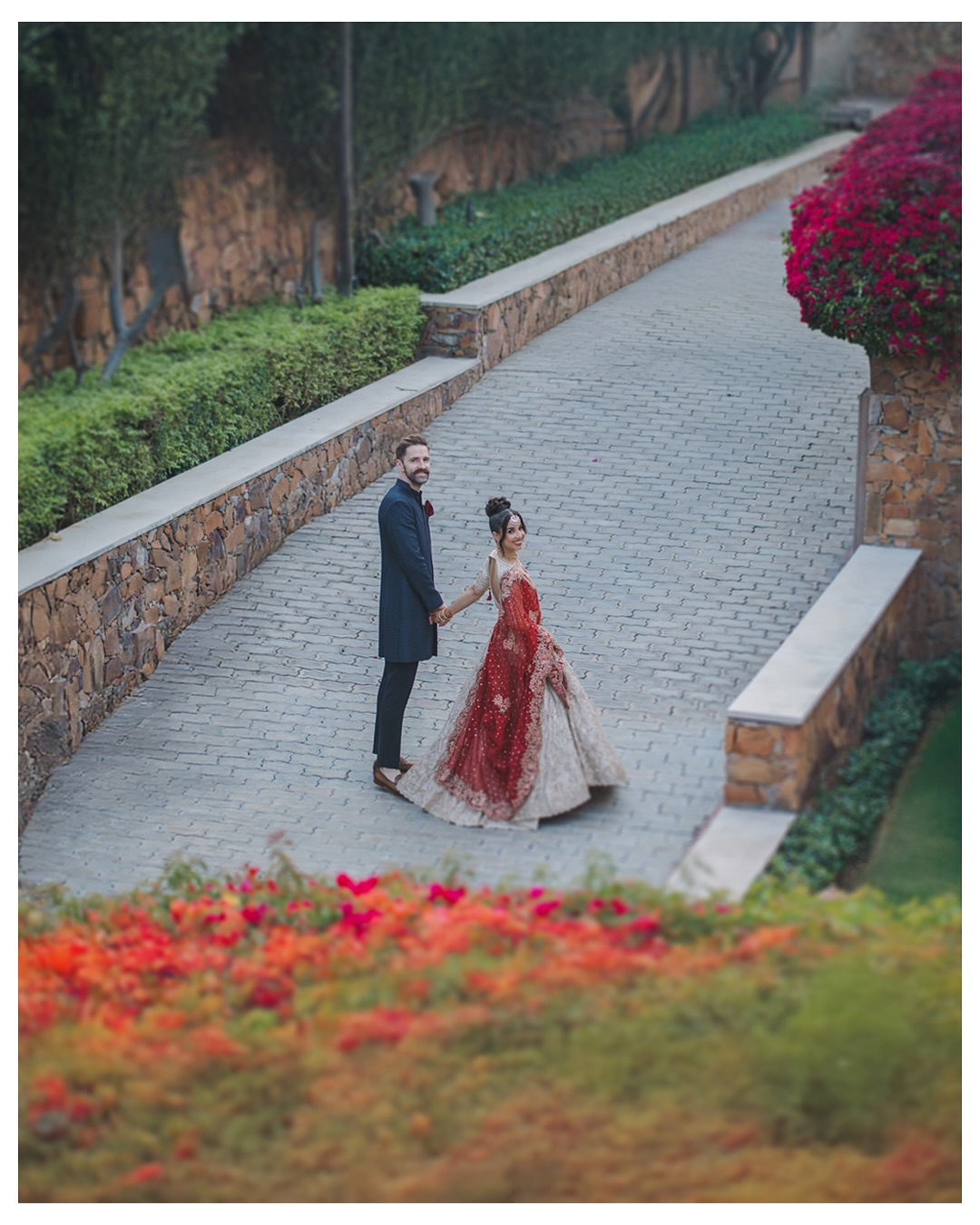 Pre wedding shoot locations Delhi - couple in red lehenga and navy suit on a stone garden path, by 7thSky Productions