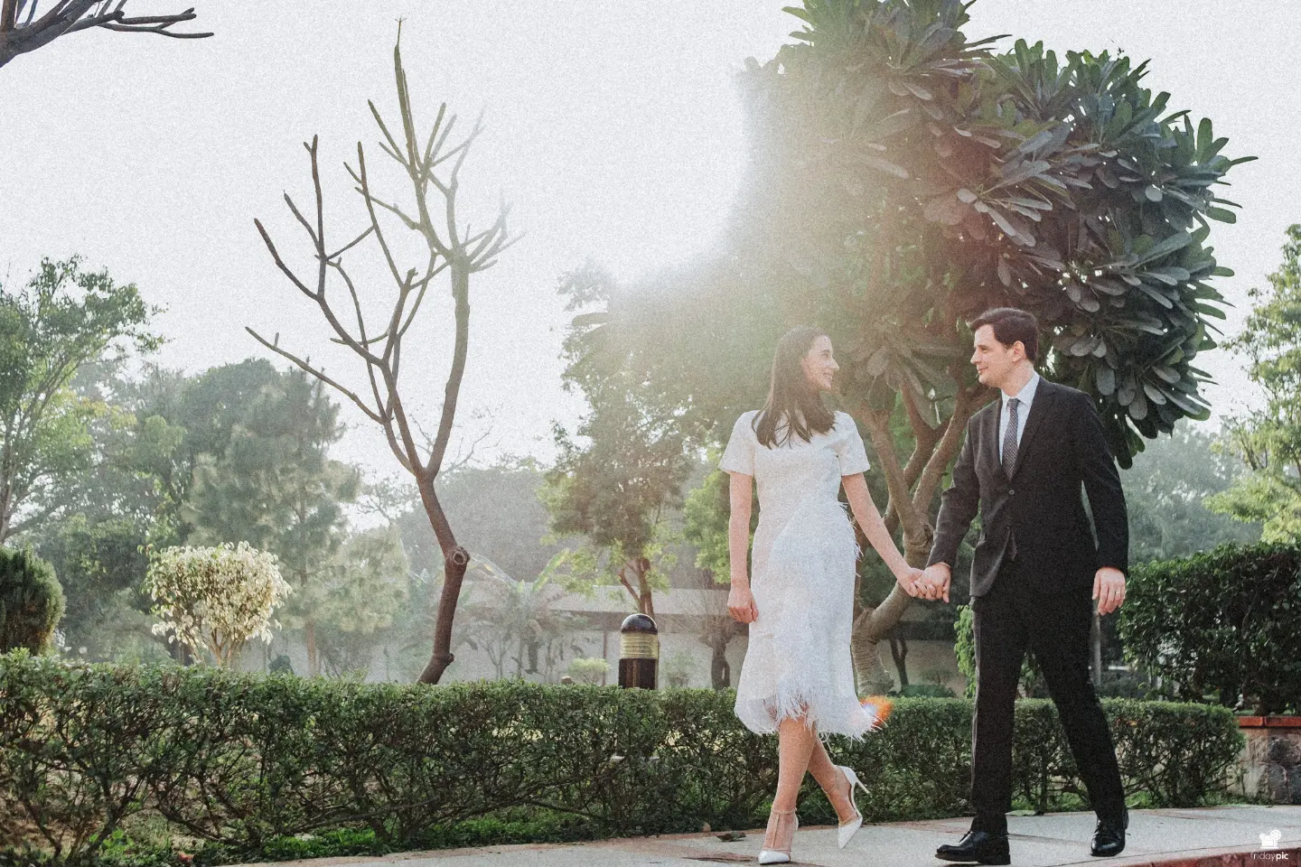 Pre wedding shoot packages Delhi - couple in white walking in a garden, by Fridaypic