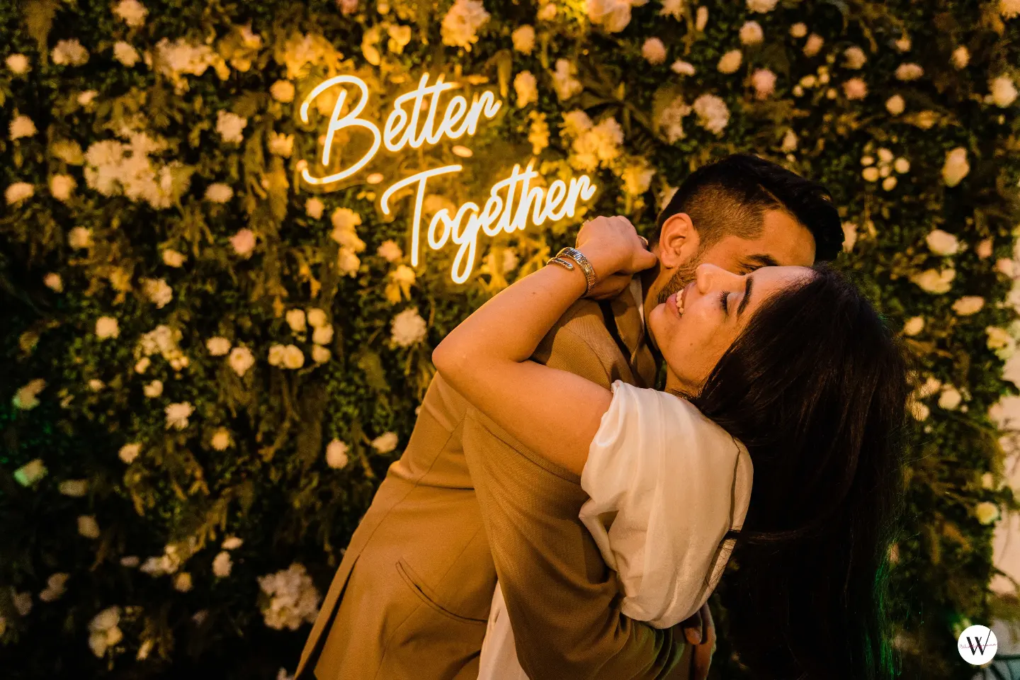 Pre wedding photoshoot at a themed set in Delhi NCR - couple hugging in front of a flower wall with a neon sign